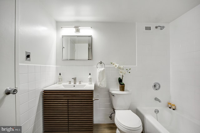 full bathroom with vanity, tiled shower / bath combo, tile walls, and toilet