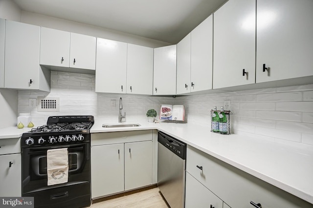 kitchen featuring dishwasher, black gas range, white cabinetry, and sink