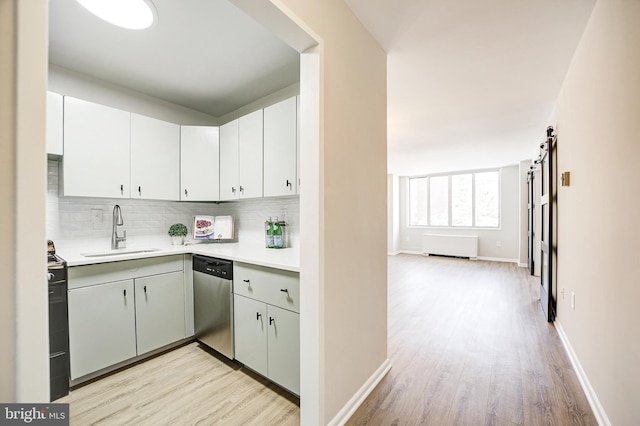 kitchen with tasteful backsplash, stainless steel dishwasher, sink, a barn door, and white cabinets