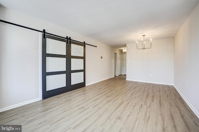 unfurnished room with a barn door, light wood-type flooring, and an inviting chandelier