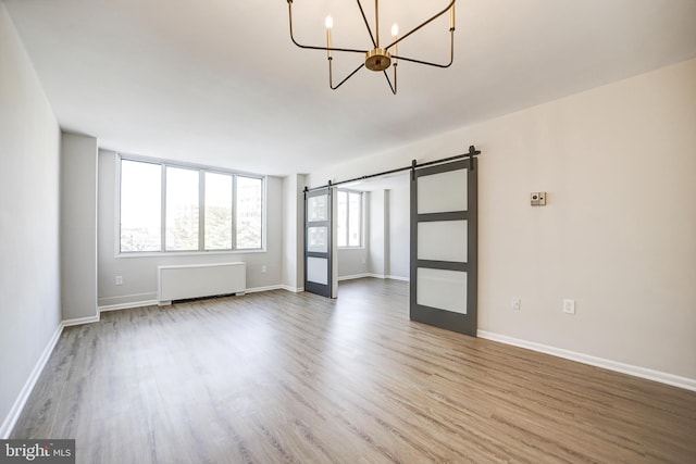 spare room with radiator heating unit, a barn door, a notable chandelier, and wood-type flooring