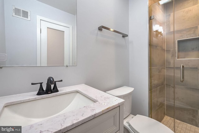 bathroom featuring a shower with door, vanity, and toilet