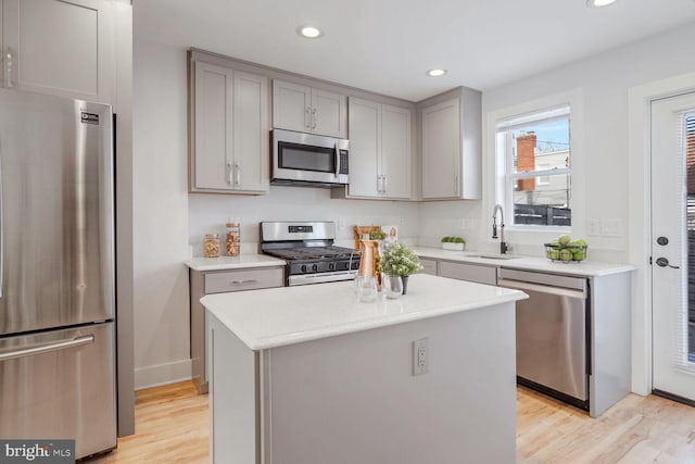 kitchen featuring sink, gray cabinets, stainless steel appliances, light hardwood / wood-style floors, and a kitchen island