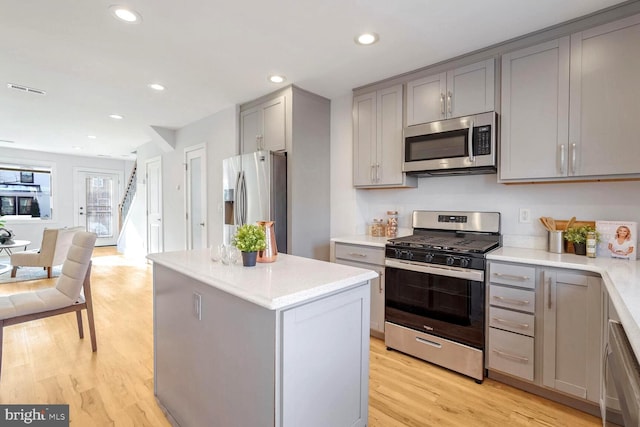 kitchen with stainless steel appliances, gray cabinets, a kitchen island, and light hardwood / wood-style flooring