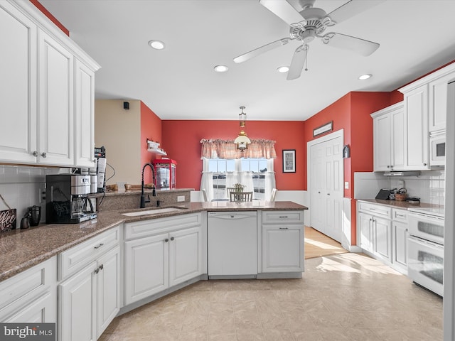 kitchen featuring white cabinets, a sink, dark stone counters, white appliances, and a peninsula