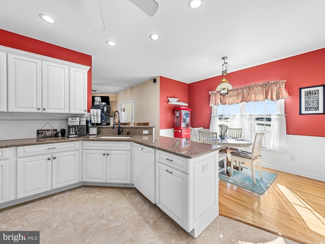 kitchen with a wainscoted wall, a peninsula, a sink, white cabinets, and dishwasher