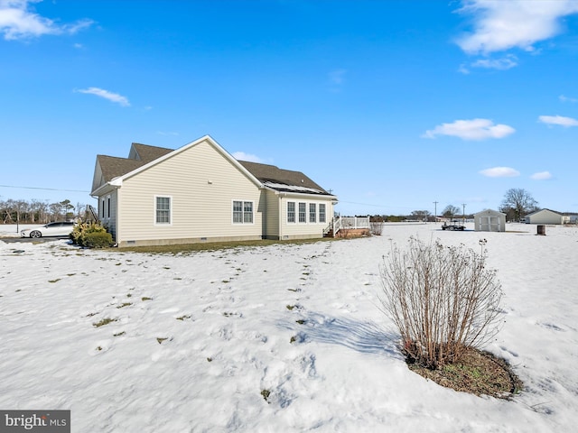 snow covered property with an outbuilding, crawl space, and a storage unit