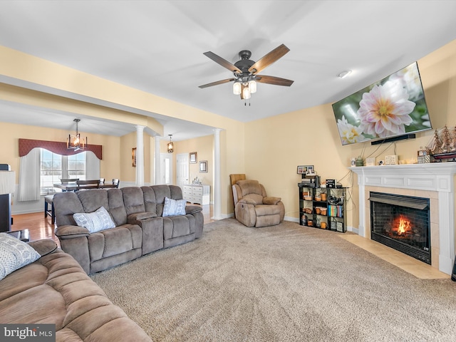 carpeted living area with a ceiling fan, a tile fireplace, decorative columns, and baseboards