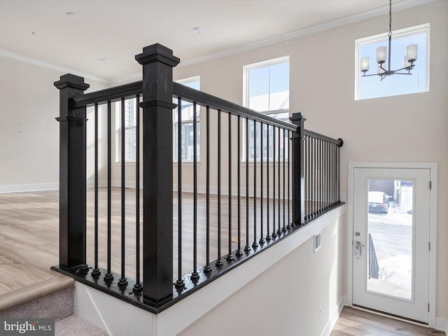 stairway with ornamental molding, a healthy amount of sunlight, a chandelier, and hardwood / wood-style flooring