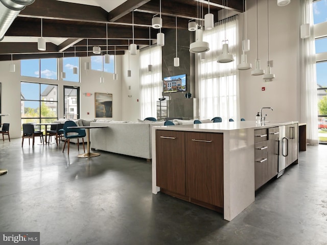 kitchen featuring beam ceiling, decorative light fixtures, a kitchen island with sink, and a towering ceiling