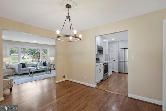 kitchen with dark wood-type flooring, hanging light fixtures, stainless steel appliances, tasteful backsplash, and white cabinets