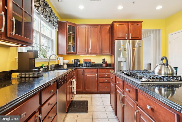 kitchen with light tile patterned floors, appliances with stainless steel finishes, sink, and dark stone countertops