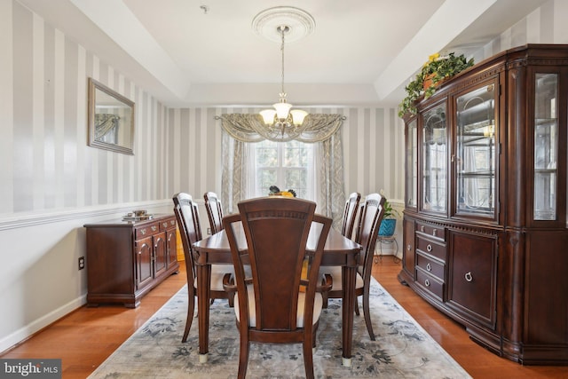 dining space with light hardwood / wood-style flooring, a raised ceiling, and a chandelier