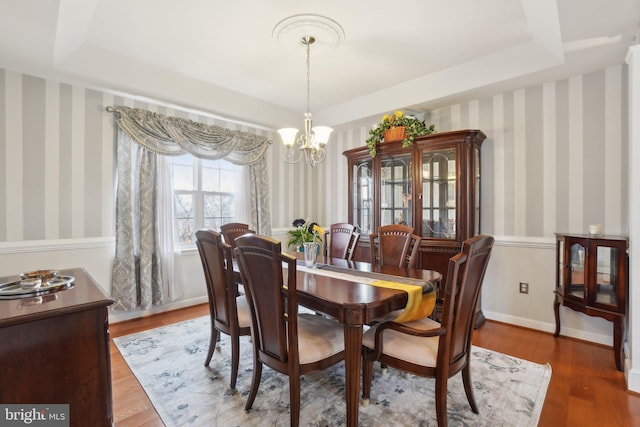 dining area with dark wood-type flooring, a chandelier, and a raised ceiling