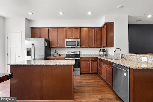 kitchen featuring sink, dark wood-type flooring, light stone counters, kitchen peninsula, and appliances with stainless steel finishes