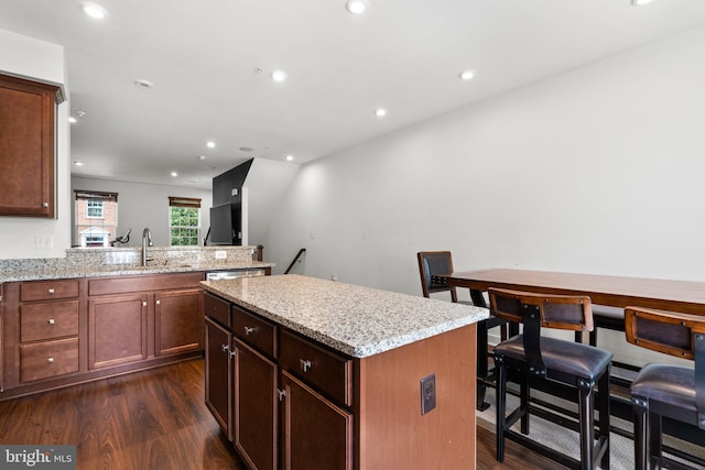 kitchen with light stone counters, a center island, dark wood-type flooring, and sink