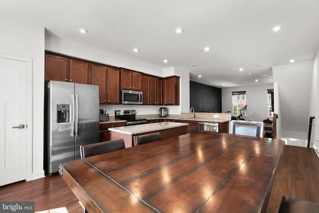 kitchen with dark hardwood / wood-style flooring, light stone counters, dark brown cabinetry, stainless steel appliances, and a center island