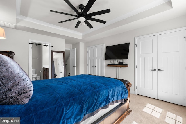 carpeted bedroom featuring a tray ceiling, ensuite bath, and ceiling fan