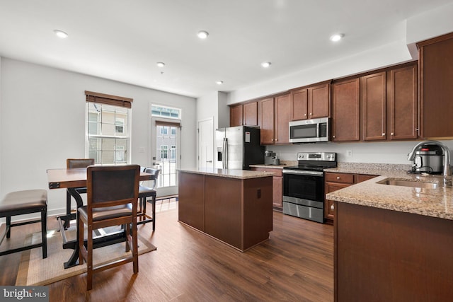 kitchen with light stone counters, stainless steel appliances, dark wood-type flooring, sink, and a kitchen island