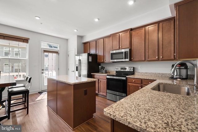 kitchen with light stone counters, stainless steel appliances, sink, dark hardwood / wood-style floors, and a kitchen island