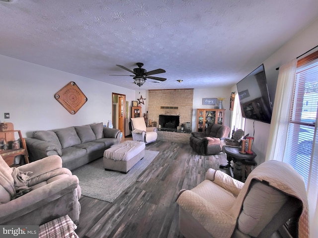 living room with a textured ceiling, a stone fireplace, ceiling fan, and dark wood-type flooring