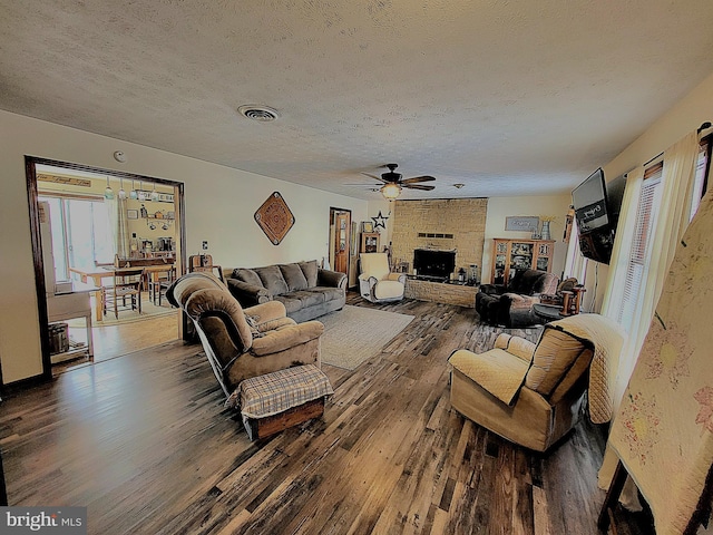 living room with ceiling fan, a large fireplace, dark hardwood / wood-style flooring, and a textured ceiling