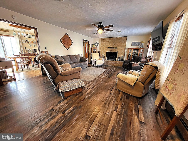 living room with ceiling fan, a large fireplace, dark hardwood / wood-style floors, and a textured ceiling