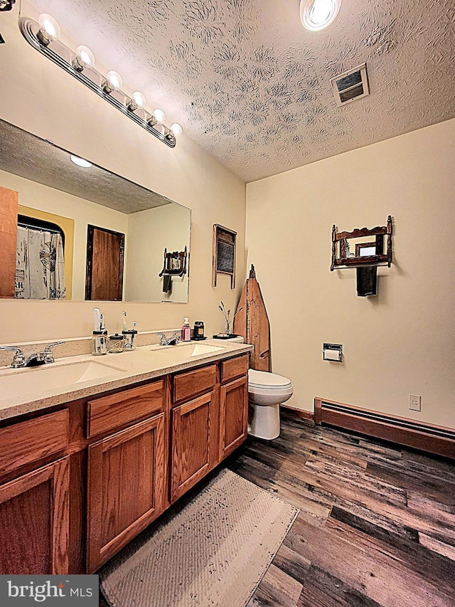 bathroom with a baseboard heating unit, wood-type flooring, a textured ceiling, toilet, and vanity