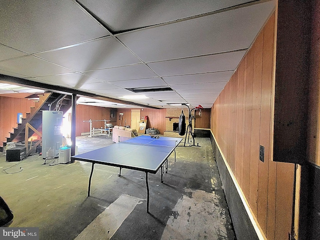 recreation room featuring a paneled ceiling, wooden walls, and concrete floors