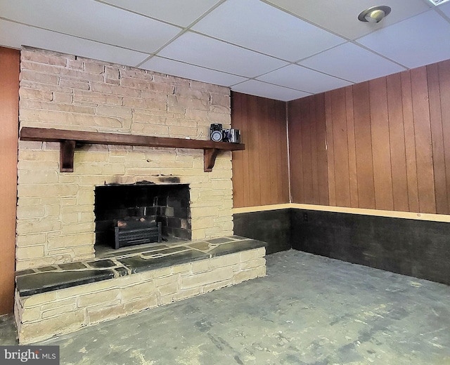 interior space featuring a drop ceiling, wood walls, concrete flooring, and a fireplace