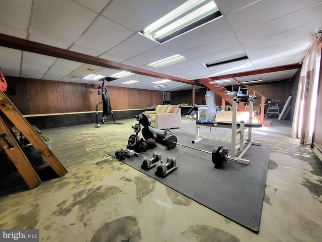 exercise room with a paneled ceiling and wood walls