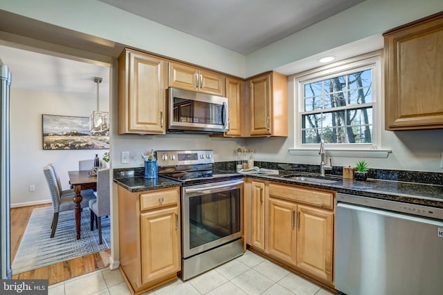 kitchen with dark stone countertops, sink, light tile patterned floors, and stainless steel appliances