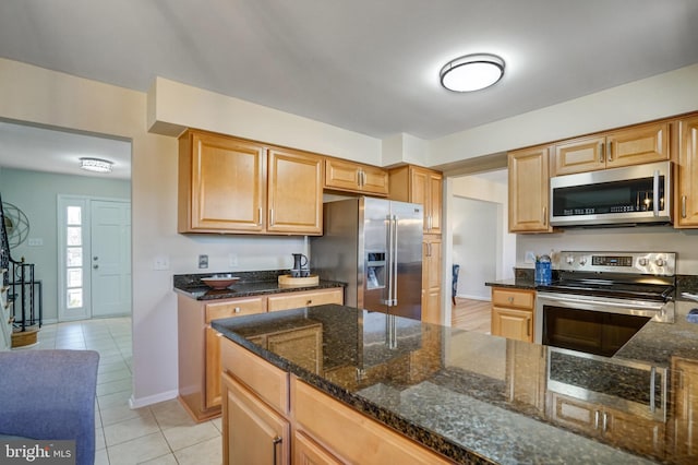 kitchen with light tile patterned flooring, appliances with stainless steel finishes, and dark stone counters