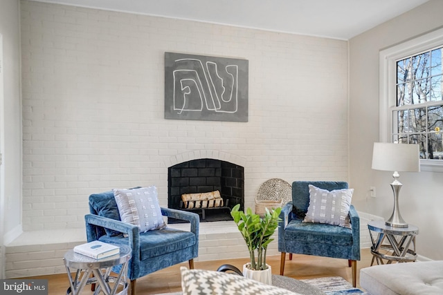 living area featuring a fireplace, wood-type flooring, and brick wall