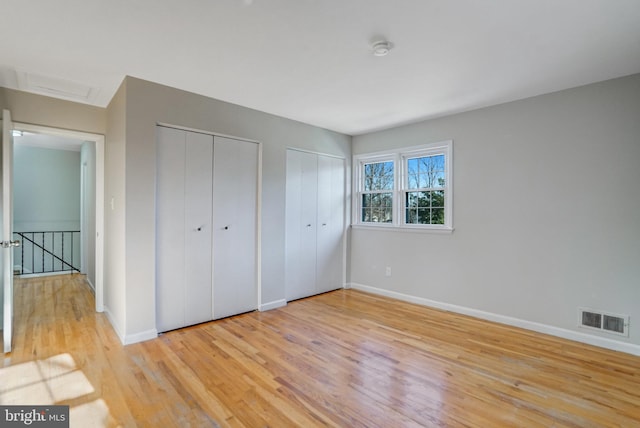 unfurnished bedroom featuring two closets and light wood-type flooring