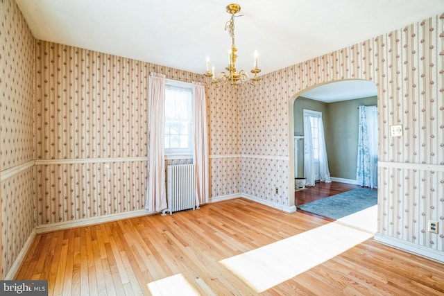 empty room with hardwood / wood-style floors, radiator heating unit, and a chandelier