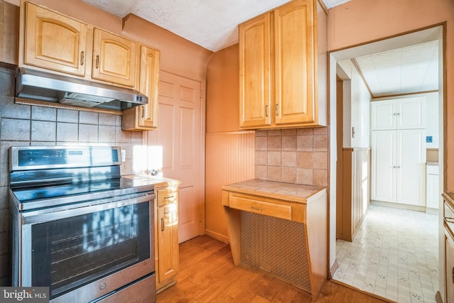 kitchen with decorative backsplash, light brown cabinetry, ventilation hood, tile countertops, and stainless steel electric range