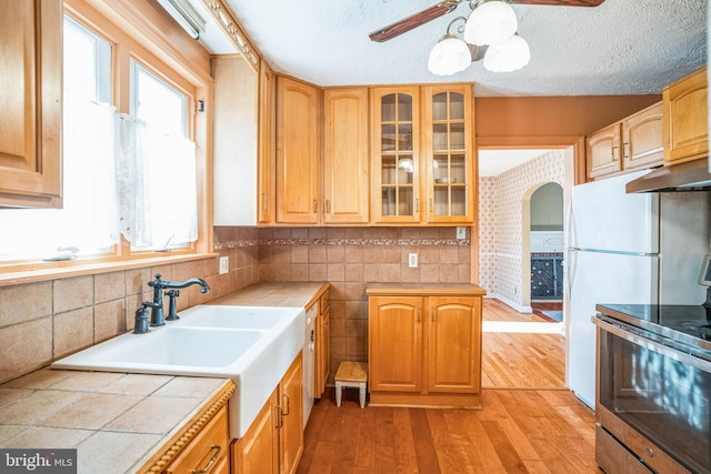 kitchen featuring ceiling fan, sink, tile counters, range, and light wood-type flooring