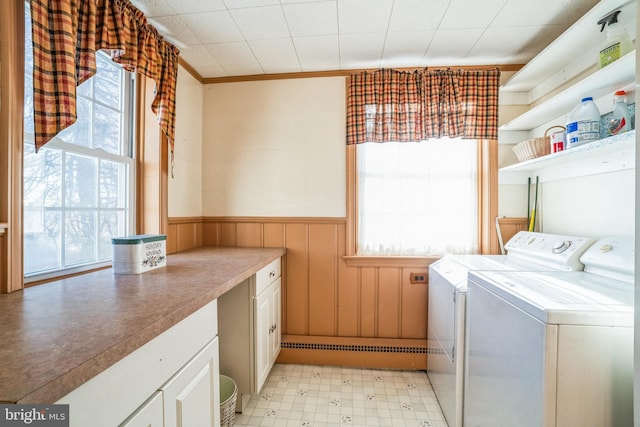 clothes washing area featuring washing machine and clothes dryer, a wealth of natural light, wood walls, and ornamental molding