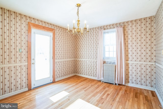 empty room featuring radiator, a healthy amount of sunlight, hardwood / wood-style floors, and a chandelier