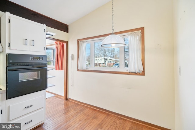 kitchen featuring light wood-type flooring, vaulted ceiling, pendant lighting, white cabinets, and black oven