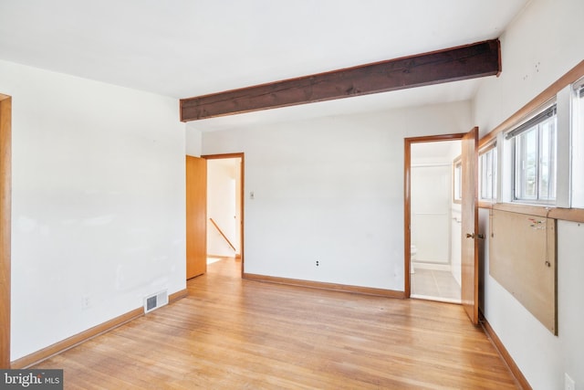 spare room featuring beam ceiling and light hardwood / wood-style floors