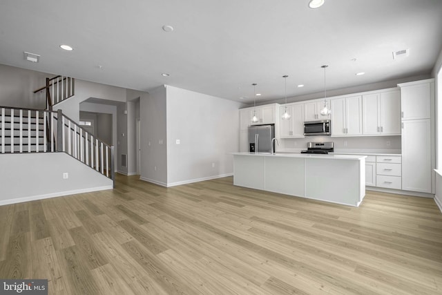 kitchen featuring appliances with stainless steel finishes, a kitchen island with sink, pendant lighting, white cabinets, and light hardwood / wood-style floors