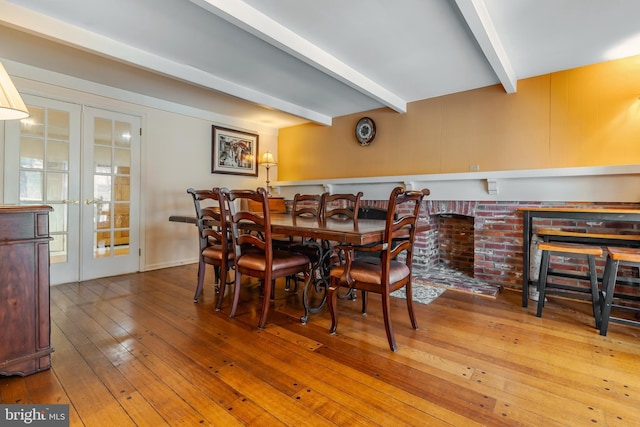 dining space with a fireplace, french doors, beamed ceiling, and hardwood / wood-style flooring