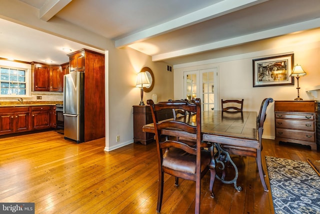 dining space with french doors, beamed ceiling, and light hardwood / wood-style floors