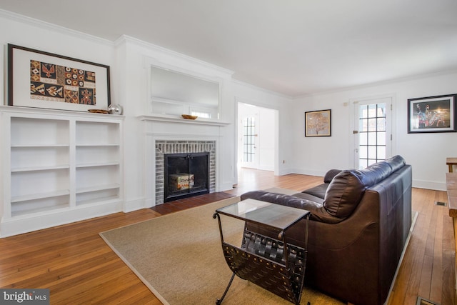 living room featuring a fireplace, built in features, ornamental molding, and hardwood / wood-style flooring