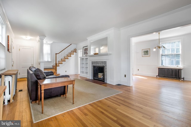 living room with a brick fireplace, ornamental molding, light hardwood / wood-style flooring, a chandelier, and radiator heating unit