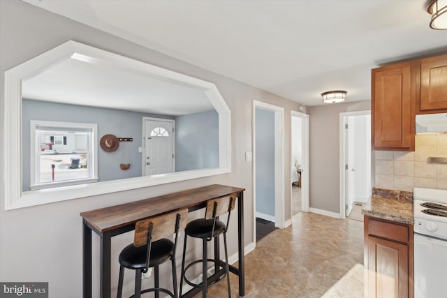 kitchen with light stone countertops, tasteful backsplash, white range oven, exhaust hood, and a breakfast bar area