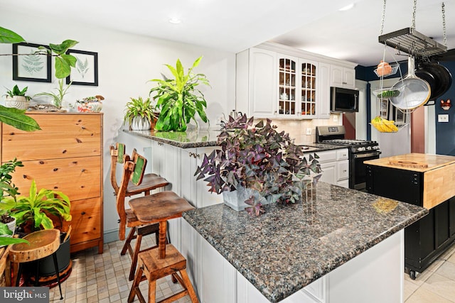 kitchen featuring backsplash, white cabinets, a kitchen island, a kitchen bar, and stainless steel range with gas stovetop