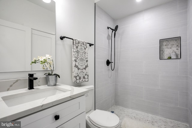 bathroom featuring a tile shower, vanity, and toilet